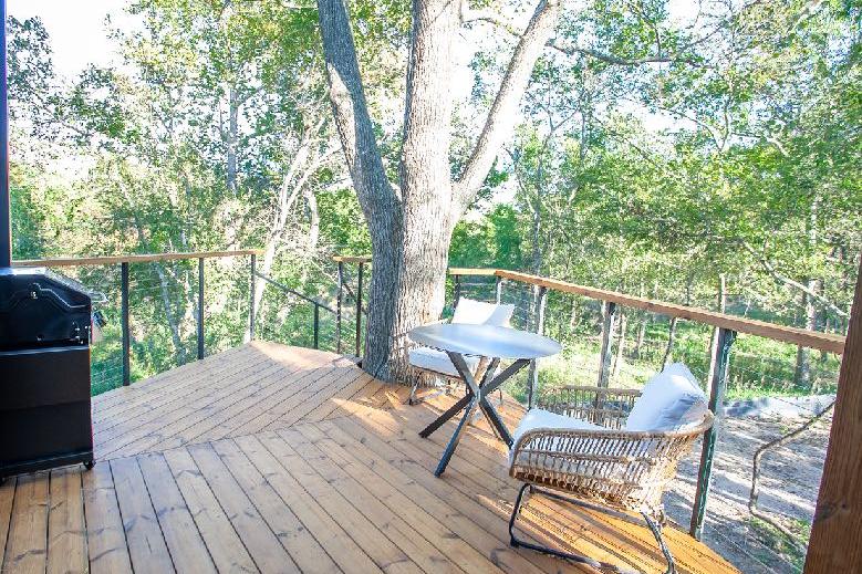 A timber deck with cable railing and outdoor seating, open to a leafy tree canopy
