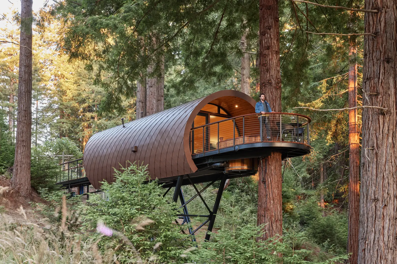 A copper barrel-vaulted treehouse cabin raised among mature redwoods