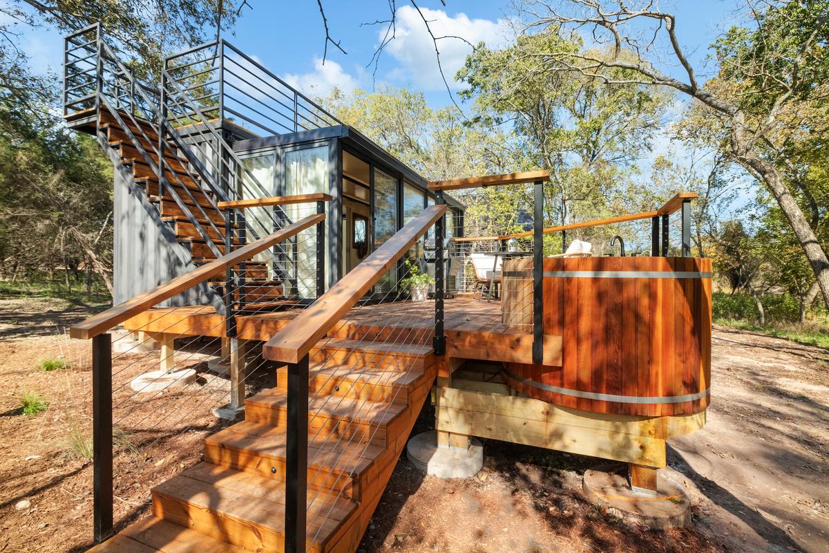 A glass-and-steel cabin with an external stair and a copper soaking tub on its timber deck