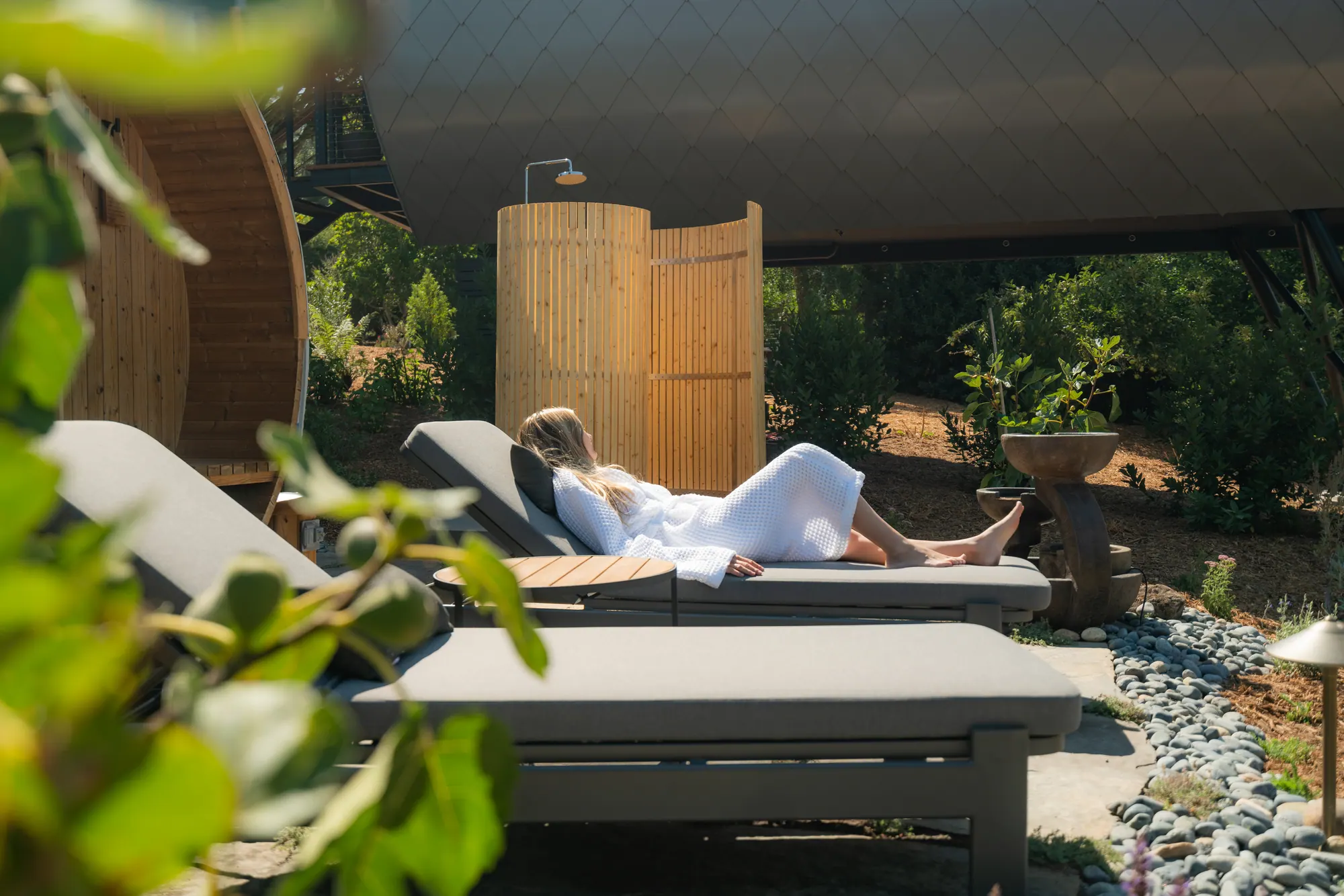 A guest resting on a daybed in an open-sided pavilion looking out to planting and stone
