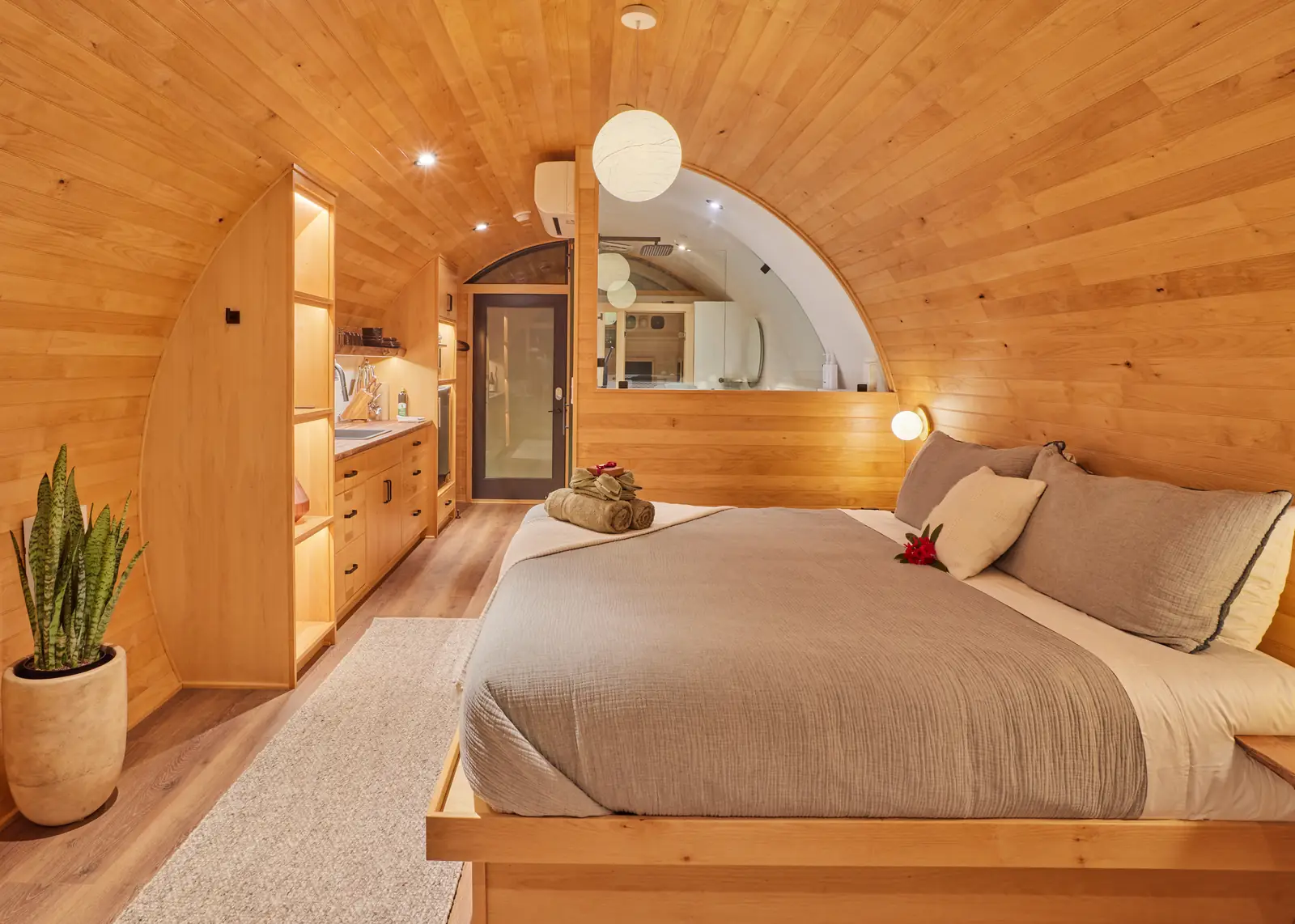 A warm timber bedroom with a curved ceiling, built-in cabinetry and an arched window