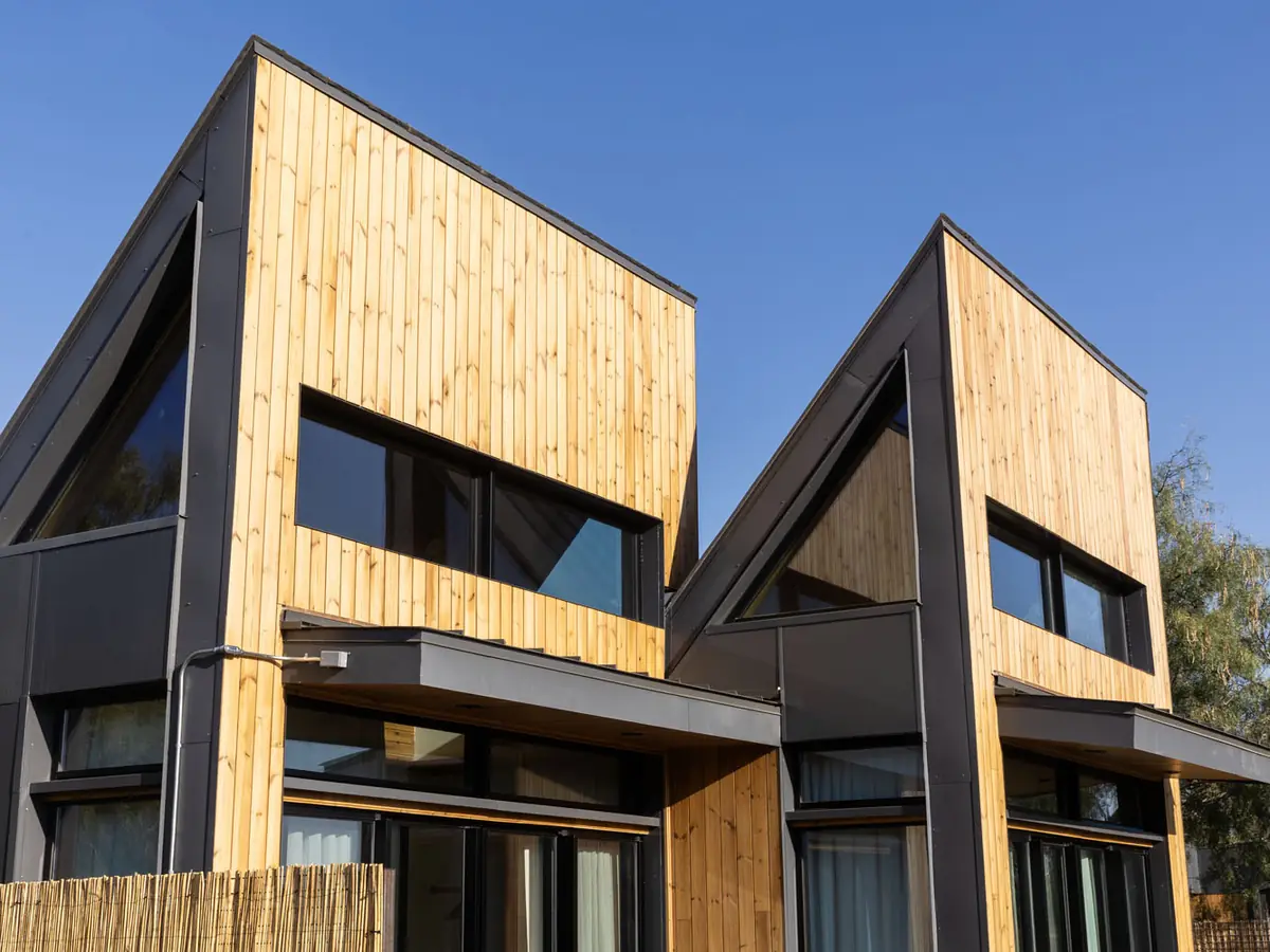 Two angular timber-clad cabins with black trim and full-height windows, under a clear sky